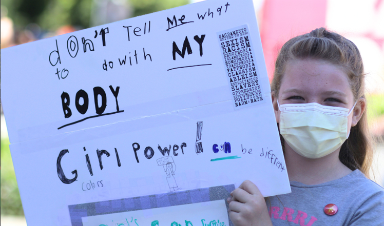 Young girl wearing a mask and holding a protest sign